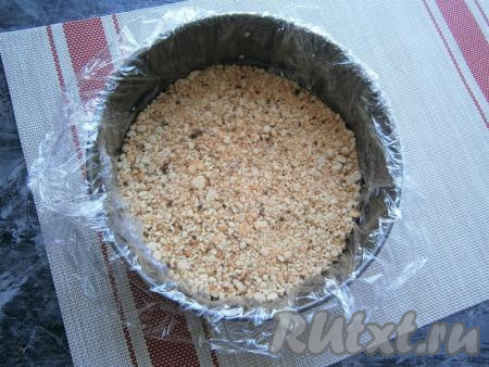 Крошку поместить в разогретую сухую сковороду и обжаривать на небольшом огне, постоянно помешивая, до румяности и готовности (для этого понадобится около 15 минут). Крошку остудить. Теперь нужно собрать торт, который будет состоять из 5 слоёв. Крошку можно разделить на 5 частей, каждая - весом около 80 грамм. Разъёмную форму диаметром 18 см полностью застелить пищевой плёнкой, дно смазать немного кремом и выложить одну часть крошки, разровнять её.