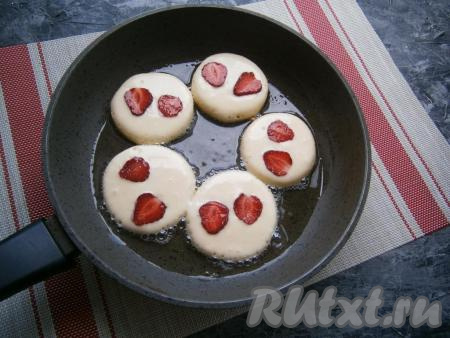 Тесто выкладывать столовой ложкой в виде оладий в сковороду с разогретым растительным маслом, сверху каждого оладушка выложить по 2 части клубнички.