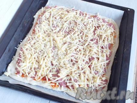 Поверх колбасы натрите сыр, равномерно распределяя его. Сверху присыпьте, по вкусу, специями. Поставьте пиццу выпекаться в разогретую до 180 градусов духовку на 20 минут (ориентируйтесь на свою духовку!).