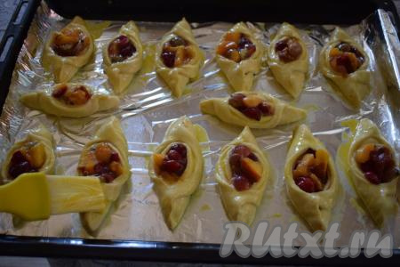 Выкладываем подготовленные пирожки с абрикосами и вишней на противень, застеленный фольгой (или пергаментом). Пирожки при помощи кулинарной кисти смазываем яйцом, взбитым вилкой с молоком. 