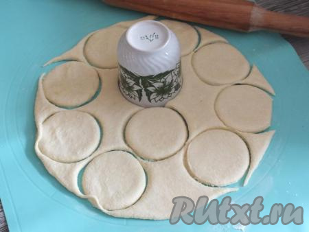 По прошествии 1,5 часов достаньте тесто из холодильника. Припылите рабочую поверхность 1 столовой ложкой без горки муки. Раскатайте тесто в пласт толщиной 0,5 см. С помощью бокала (или стакана) вырежьте кружочки. Обрезки теста соберите, рабочую поверхность можно ещё немного припылить мукой, опять раскатайте оставшееся тесто и опять вырежьте кружочки. И так до тех пор, пока не закончится тесто.