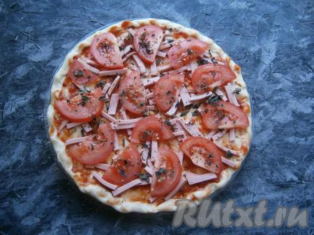 Колбасу нарезать брусочками (или кружочками), выложить по всей лепешке. Сверху разместить полукружочки свежих помидоров, посыпать начинку сушёным базиликом и чёрным молотым перцем.