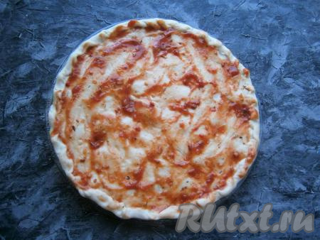 Затем тесто раскатать (или растянуть руками) в лепёшку, равную диаметру стеклянной тарелке из микроволновки, разместить лепёшку на этой тарелке. По желанию, сформировать небольшие бортики. Смазать лепёшку томатным соусом (или кетчупом).
