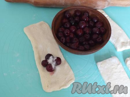 На каждую заготовку, ближе к одному из краёв,&nbsp;выложите 4-5 ягод вишни. Присыпьте начинку чайной ложкой сахара.