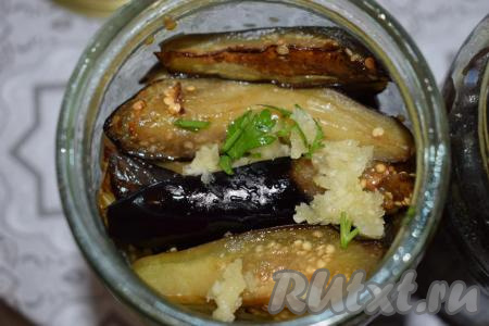 Раскладываем горячие баклажаны равномерно по банкам. Сверху кладём оставшиеся чесночок и петрушку.