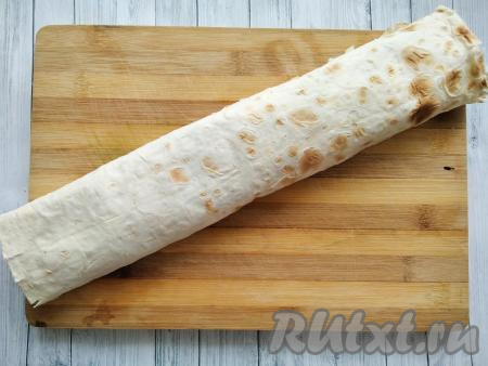 Свернуть лаваш в плотный рулет, скручивая широкую сторону лаваша. Завернуть рулет в пищевую плёнку и поместить в прохладное место (или в холодильник) минут на 30 для пропитки.