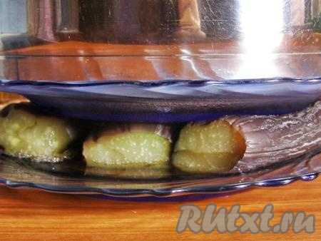 Перекладываем баклажаны на плоскую тарелку. Накрываем сверху тарелкой, на которую ставим небольшую кастрюлю (или банку) с водой, оставляем баклажаны под прессом на час. Жидкость, которая будет выделяться из баклажанов, нужно сливать.