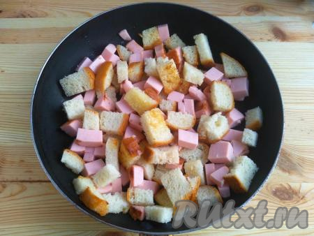 На сковороду влить 1 столовую ложку растительного масла, выложить кусочки колбасы и батона, обжарить их на среднем огне до лёгкого зарумянивания, постоянно помешивая.