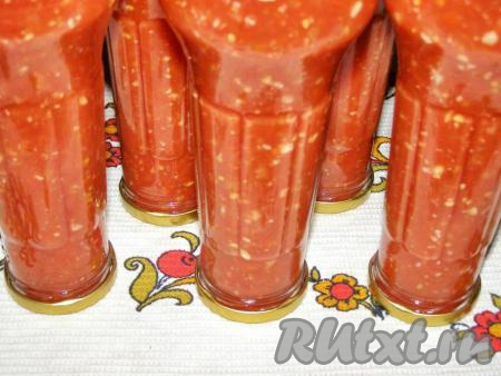 Когда аджика из помидоров, чеснока и перца закипит, варим её 5 минут и в горячем состоянии переливаем в заранее простерилизованные бутылки или банки. Закручиваем прокипячёнными крышками и ставим вверх дном. Оставляем в таком виде, пока аджика не остынет.