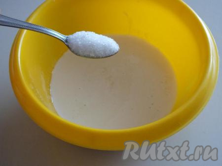 Для приготовления оладий нам потребуется ряженка комнатной температуры, поэтому из холодильника её нужно достать заранее. Ряженку комнатной температуры налейте в просторную миску, добавьте щепотку соли и 1 чайную ложку сахара, перемешайте.