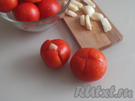 Помидоры вымойте. Сделайте крестообразный разрез в верхней части каждого плода, не дорезая до конца. В отверстие вложите по 1-2 кусочка&nbsp;чеснока.