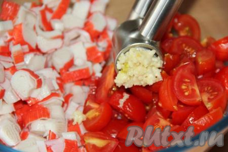 Очищенный зубчик чеснока пропустить через пресс и выложить к крабовым палочкам и помидорам.