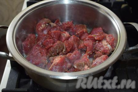 Далее берём толстостенную кастрюлю и разогреваем её на огне. Вливаем в кастрюлю растительное масло и добавляем сливочное. Выкладываем в разогретое масло кусочки говядины&nbsp;и жарим, постоянно помешивая, примерно, 10 минут на среднем огне.