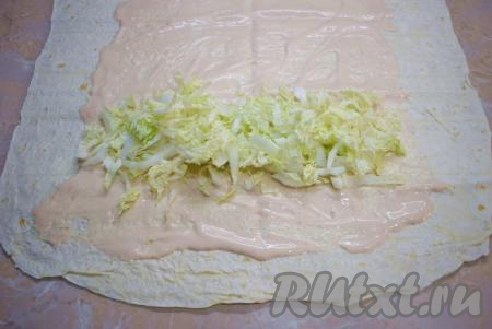 Теперь можно приступать к сборке домашней шаурмы, для этого разложите на столе лист лаваша и смажьте его 1/4 частью получившегося соуса, немного не доходя до краёв лаваша. С одной стороны, отступив от края, выложите 1/4 часть пекинской капусты.