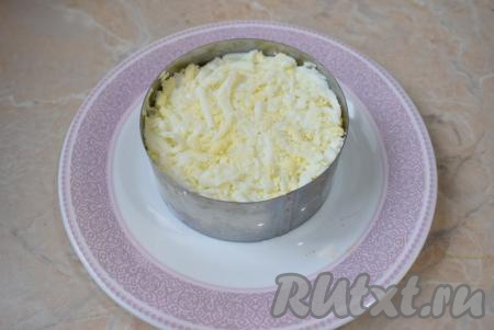 Отварные яйца очистите от скорлупы и натрите на крупной тёрке. Выложите их в салатник. Немного прижмите, чтобы слой стал более плотным. Смажьте яйца небольшим слоем майонеза.