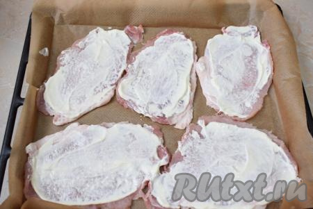 Противень для запекания застелите пергаментом и выложите на него отбитое мясо. Каждый кусочек смажьте небольшим количеством майонеза (он придаст мясу сочность). Вместо майонеза можно воспользоваться сметаной.