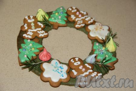 Немного глазури оставить для формирования рождественского венка. На остывшее кольцо из пряничного теста точечно нанести глазурь, поверх которой выложить пряники и аккуратно прижать (пряники приклеятся). С помощью глазури можно прикрепить и разноцветные небольшие меренги, они тоже отлично смотрятся на рождественском венке. Пока глазурь на пряниках не высохла, их можно посыпать различной кондитерской посыпкой. Оставить подсохнуть на пару часов (до полного высыхания).