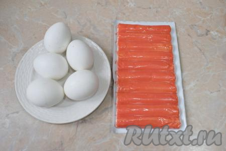 Крабовые палочки извлеките из морозильной камеры и дайте полежать при комнатной температуре, чтобы они разморозились. Отварите яйца вкрутую (варите в кипящей воде в течение 7-8 минут), затем горячую воду с них слейте и остудите в холодной воде.