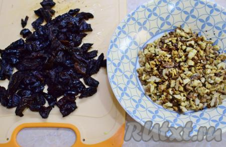 Чернослив залейте кипятком минут на 5, затем промойте его пару раз в холодной воде, обсушите и мелко нарежьте. Ядрышки грецких орехов порубите ножом и обжарьте на сухой сковороде на среднем огне в течение нескольких минут (до появления характерного аромата), после этого пересыпьте на тарелку и остудите.