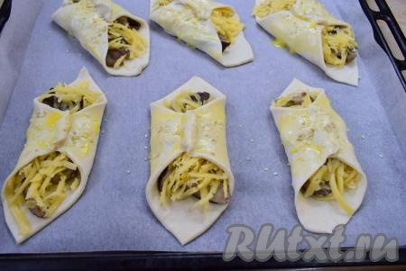 Противень для выпечки застелите пергаментом и выложите на него подготовленные слойки с грибами и сыром. Тесто смажьте яичным желтком и посыпьте кунжутом. Поставьте противень в духовку, разогретую до 180 градусов, на 30-35 минут (ориентируйтесь по своей духовке).