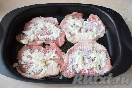Лук очистите от шелухи, ополосните, затем мелко нарежьте. На каждый кусочек мяса выложите нарезанный лук. Немного смажьте майонезом кусочки свинины с луком.