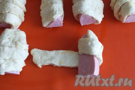Каждый ломтик колбасы оберните полоской из теста. Обёртывая, слегка вытягивайте тесто, делая небольшой нахлёст. 
