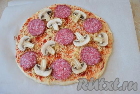Колбасу нарежьте тонкими ломтиками. Тесто посыпьте сыром, натёртым на мелкой тёрке (1/4 часть сыра отложите&nbsp;для посыпки сверху начинки). А затем разложите ломтики колбасы. Я дополнительно добавила в начинку пиццы дольки шампиньонов, но это по желанию. Шампиньоны использовала сырые, предварительно их ополоснув в холодной воде.
