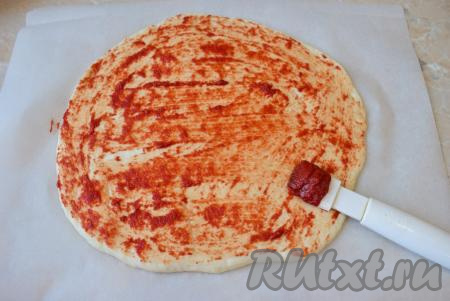 Подошедшее тесто разрежьте на 2 части (будем готовить 2 пиццы). Каждую часть теста на присыпанной мукой поверхности раскатайте в круг диаметром, примерно, 30 см. Выложите заготовки пиццы на бумагу для выпечки. Поверхность теста смажьте томатной пастой.