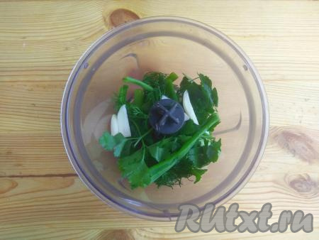 В чашу блендера выложить очищенный чеснок и произвольно нарезанную зелень.