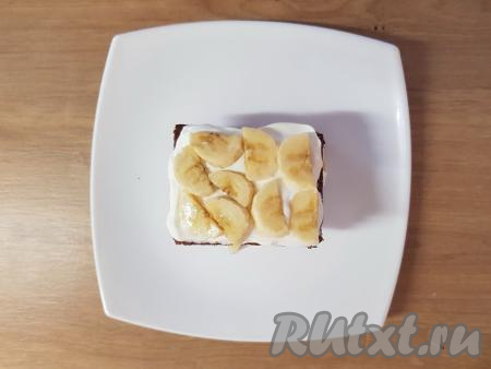 Следующим слоем выложить ещё кусочек коржа, смазанный мягким творогом.&nbsp;Сверху разложить в один слой кусочки банана.