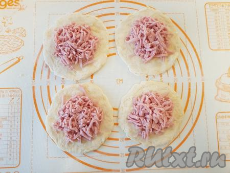 Натёртую колбасу (или сосиски) разделить на 4 равные части и выложить в центр каждого кружочка.