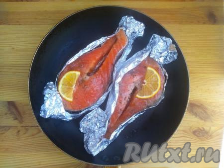 Аналогично выполнить вторую лодочку из фольги со стейком сёмги. Выложить лодочки в жаропрочную форму. На каждый стейк сёмги поместить по дольке лимона. Выпекать стейки сёмги в разогретой духовке в течение 25 минут при температуре 200 градусов.