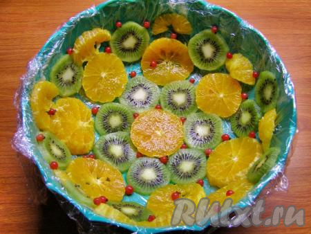 Форму для торта (диаметр формы, примерно, 20 см, глубина - 7-9 см) застилаем пищевой плёнкой, концы плёнки должны свисать с краёв формы. Выкладываем в застеленную форму кружочки фруктов и ягоды.