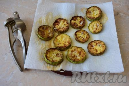 Готовые кабачки перекладывайте на тарелку, застеленную бумажными полотенцами, для того, чтобы удалить лишнее масло. На каждый кружочек горячего кабачка выложите немного измельчённого чеснока. Для измельчения чеснока удобно использовать чеснокодавилку.