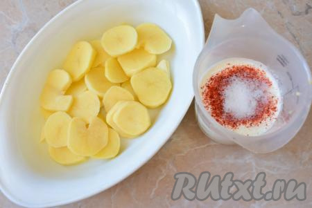 Сливки можно использовать любой жирности. Чем выше их жирность, тем насыщеннее будет сливочный вкус готового блюда. В сливки добавьте соль и специи, перемешайте. В форму для запекания выложите половину нарезанного картофеля. Полейте картофель половиной сливок.