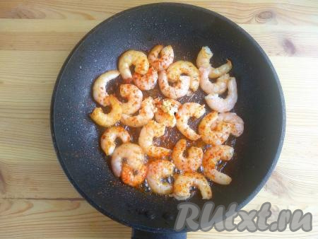 Зубчики чеснока пропустить через пресс (или натереть на средней тёрке). Перевернуть&nbsp; креветки, выложить подготовленный чеснок, добавить специи по вкусу. Продолжать готовить около 1-2 минут. Недожаренные креветки имеют вытянутую форму, пережаренные экземпляры сворачиваются в кружок. Идеально жареная креветка должна быть, как буква «С». Общее время термообработки морепродуктов не должно превышать 5 минут.