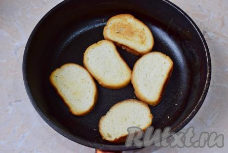 Первым делом необходимо поджарить гренки, для этого на среднем огне разогрейте сковороду, затем налейте в неё немного растительного масла, выложите ломтики батона и поджарьте их с двух сторон до золотистой, хрустящей корочки. Готовые гренки переложите со сковороды на тарелку.