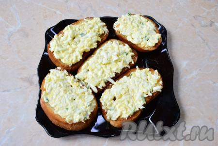 На каждый ломтик обжаренного батона выложите немного яичной намазки и равномерно её распределите по всей поверхности.