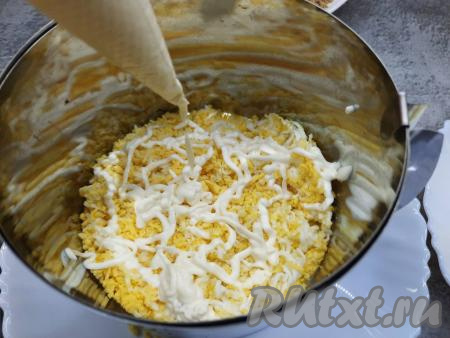 Теперь можно приступать к формированию слоёного салата. Я сформировала салат в разъёмной форме, поставив её на тарелку, можно просто выложить салат слоями в салатник. На дно формы (или салатника) первым слоем нужно выложить половину натёртых яиц, немного примять ложкой, смазать частью майонеза, смешанного с чесноком (для удобства я переложила смесь майонеза с чесноком в кондитерский мешок).&nbsp;