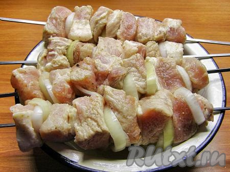 По истечении времени достаём миску с мясом из холодильника. Нанизываем кусочки свинины на металлические шампуры, чередуя с луком. Деревянные шпажки использовать не стоит, они могут сгореть от высокой температуры. По желанию, между мясом и луком можно надеть на шампур кружочек помидора.