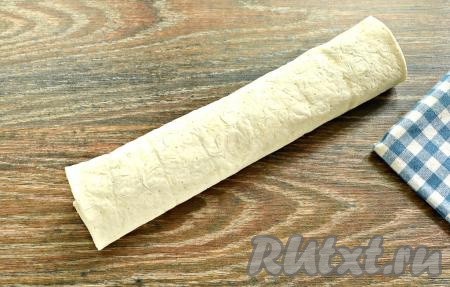 Свернуть лаваш с начинкой из шампиньонов и сыра в рулет, начиная с широкой стороны.