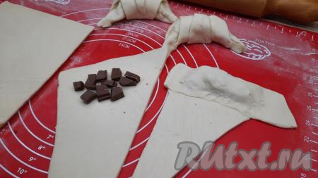 Всего у нас получатся 8 треугольников. На широкий край каждого треугольника, немного отступив от края, выложить кусочки шоколада. Накрыть шоколад широким свободным краем и хорошо придавить, чтобы шоколад в процессе выпекания не вытек. Свернуть каждый треугольник с тестом в рулетик, начиная от широкой стороны с начинкой. Придать каждому сформированному рулетику форму полумесяца.