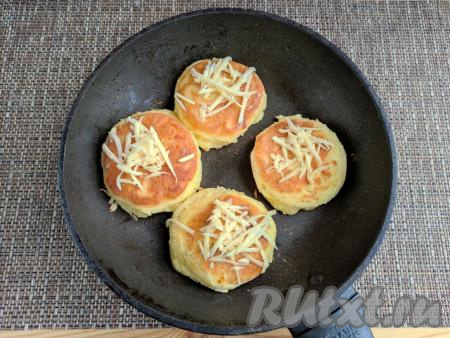 Сырники перевернуть, посыпать сверху оставшимся натёртым сыром. Накрыть сковороду крышкой, огонь убавить до минимального. Готовить ещё 5 минут.