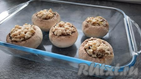 Шляпки шампиньонов, начинённые куриным фаршем, смешанным с ножками и луком, выложить в форму для запекания и отправить в разогретую до 170 градусов духовку на 20 минут.