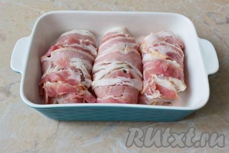 Оберните рулет полосками тонко нарезанного сырокопчёного&nbsp;бекона. Для запекания удобно использовать керамические формы. Дно и бока формы смажьте растительным маслом и выкладывайте в неё рулетики в беконе. Поставьте форму в духовку, предварительно разогретую до 180 градусов, на 40-45 минут.