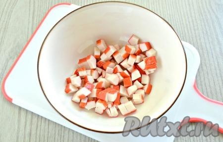 Удаляем упаковку с крабовых палочек (если палочки заморожены, их нужно полностью разморозить), нарезаем кубиками и перекладываем в салатник.