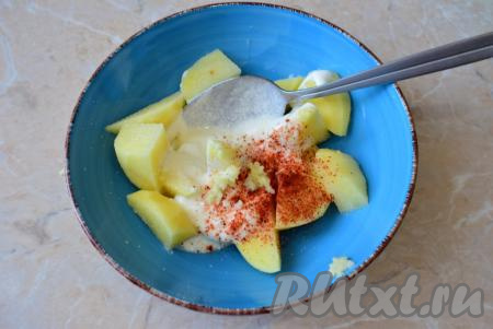 К долькам картошки добавьте сметану, соль, пропущенные через пресс зубчики чеснока и специи, перемешайте, чтобы картофель со всех сторон был равномерно покрыт сметанкой.