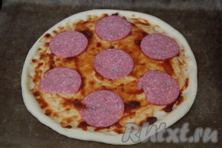 Смазать основу пиццы 2 столовыми ложками томатного соуса (или кетчупа) и выложить тонкие ломтики колбасы. Учитывайте, что количество начинки, указанной в ингредиентах, рассчитано на 2 пиццы.