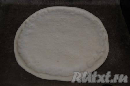 Разделить тесто на 2 части. Мы будем готовить 2 пиццы. Раскатать вначале одну часть теста скалкой в круг диаметром 30 см, переложить на противень, застеленный пергаментом. Сформировать руками на раскатанном тесте небольшой бортик, характерный для пиццы. Оставить основу для пиццы на 15 минут на противне.