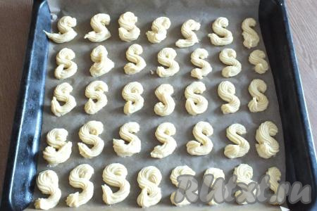 Застелите противень пекарской бумагой. Тесто выложите в кондитерский шприц (или кондитерский мешок) и отсадите на застеленный противень. Форма печенья может быть любой. Если нет шприца (или кондитерского мешка), воспользуйтесь обычной чайной ложкой. Оставьте противень с заготовками на столе на 30 минут, чтобы тесто подсохло. После поставьте в разогретую до 180 градусов духовку на 15-20 минут.